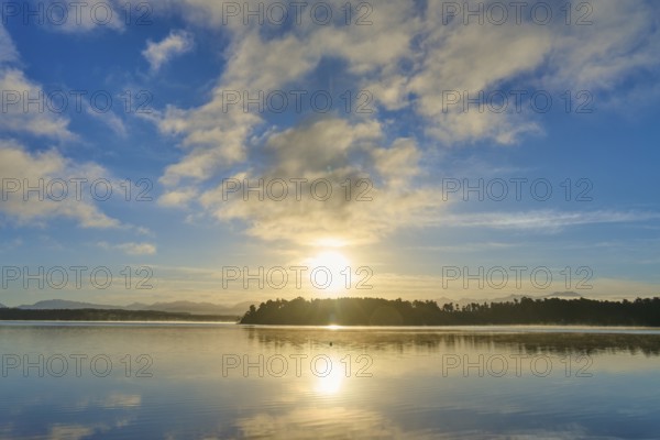 Sunlight breaks through the clouds in the morning over a calm lake, Lake Mahinapua, Ruatapu, South Island, New Zealand, Oceania