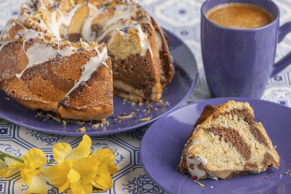 Cut marble bundt cake, cake on blue plates with icing, next to a blue cup of coffee