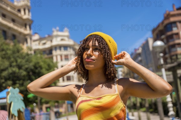 Young woman adjusting her yellow beanie in valencia city center, enjoying a sunny summer day outdoors