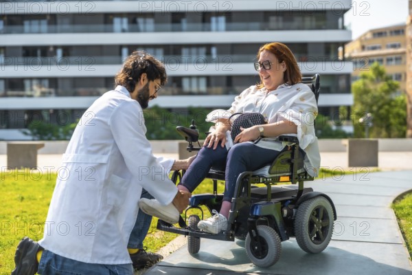 Male doctor is adjusting the footrest of an electric wheelchair for a smiling woman, promoting accessibility and healthcare in a sunny park setting