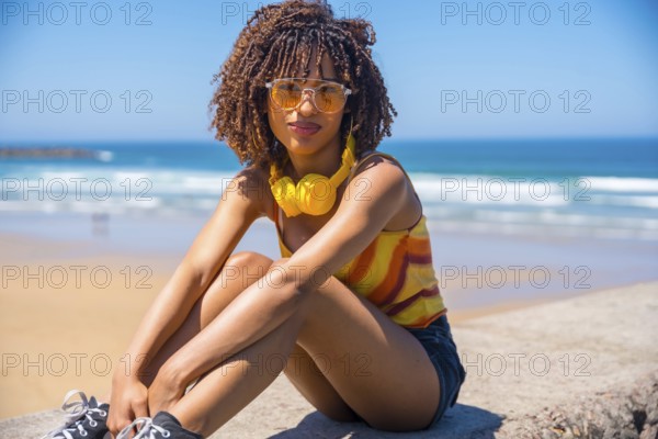 Fashionable young woman enjoying the summer sun and music on a beach wall, embracing the carefree vibes of vacation