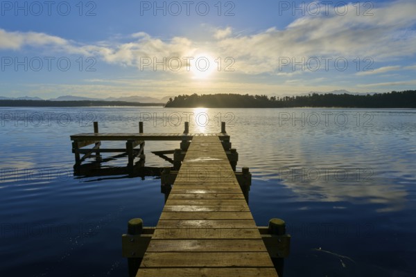 A jetty leads into a lake, the sun shines brightly and is reflected in the water, Lake Mahinapua, Ruatapu, South Island, New Zealand, Oceania