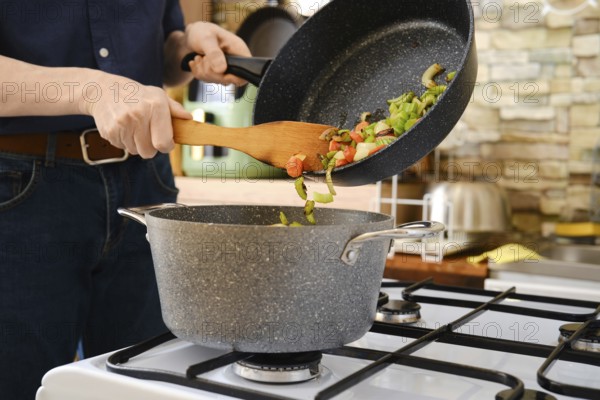 Unrecognizable person shifts stir-fried vegetables into the pot from a frying pan on the stove