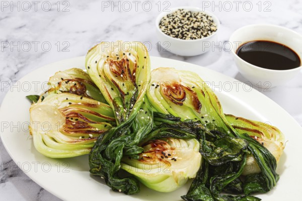 Grilled bok choy served with soy sauce and sesame seeds, on a white plate, homemade, no people