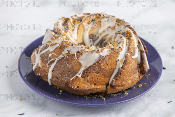 Marble bundt cake, cake with icing and edible flowers on a blue plate, light background