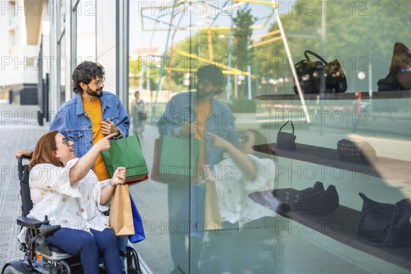 Happy friends doing shopping and looking at a shop window, a disabled woman on a wheelchair is pointing at a bag
