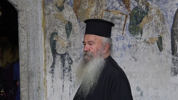 Priest in clerical garb in front of a religious mural, Monastery of St John the Theologian, Monastery of St John the Theologian, World Heritage Site 1999, Patmos, Dodecanese, Greek Islands, Greece, Europe