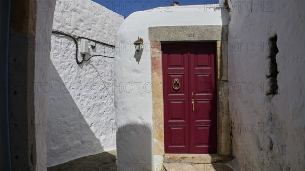 A winding entrance with a striking red door and stone walls, illuminated by a small lantern, Mantomata Stones, Chora, UNESCO World Heritage Site 1999, Patmos, Dodecanese, Greek Islands, Greece, Europe