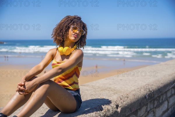 Young woman soaking up the summer sun and ocean breeze, enjoying music through her headphones while relaxing on the beach