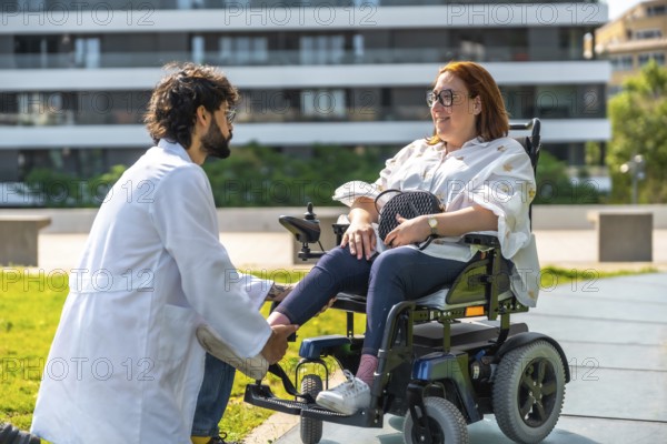 Doctor adjusting the footrest of an electric wheelchair for a smiling woman, enjoying a sunny day in the park surrounded by greenery