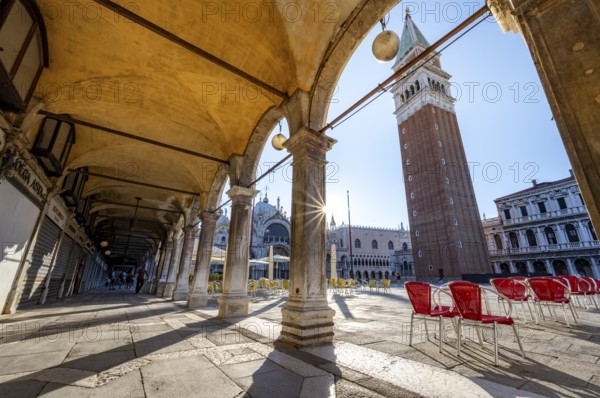 Chairs and tables of cafes, arcades at St Mark's Square in the morning light, St Mark's Basilica and Campanile, Sun Star, Venice, Veneto, Italy, Europe