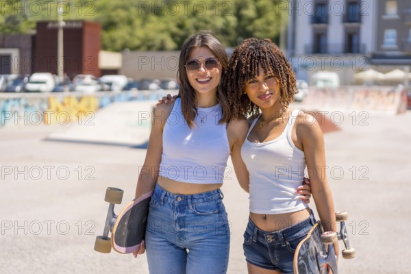 Two young women smiling and holding skateboards, enjoying their time together in a vibrant skatepark under the sunny summer sky