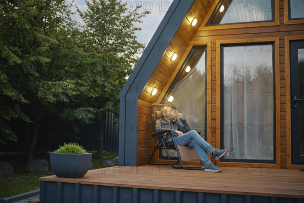A relaxed senior man sits thoughtfully at sunset on the terrace and smokes a cigar