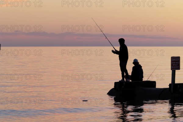 Silhouette of young adults ignoring danger sign while fishing on storm drain culvert in Long Beach, Mississippi, USA, North America
