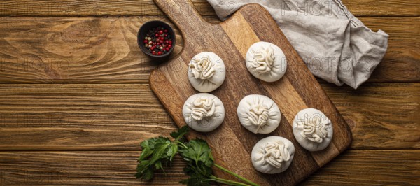 Raw freshly made Khinkali, traditional dish of Georgian Caucasian cuisine, dumplings filled with ground meat on white plate with herbs on wooden rustic background table top view space for text