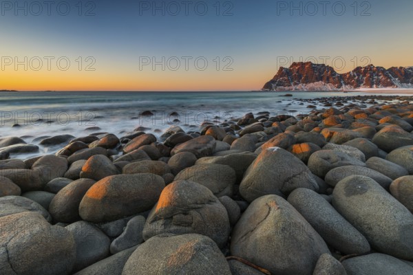The famous beach near Uttakleiv with round shaped rock boulders on the Lofoten islands in Norway on clear winter day with snow-clad mountains and blue sky after sunset