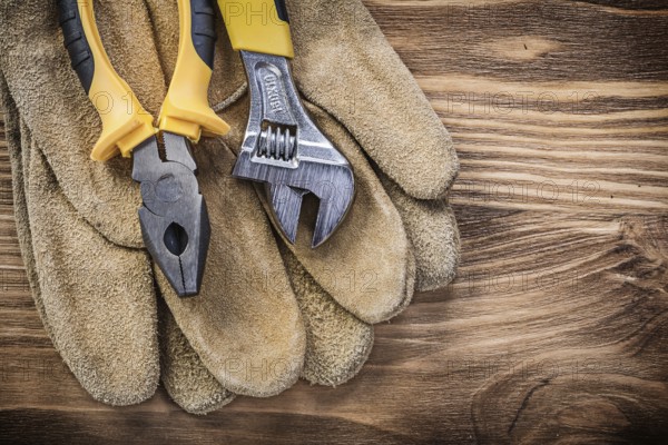 Leather safety gloves adjustable spanner pliers on wooden board construction concept