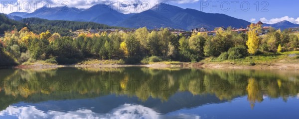 Bansko, Bulgaria autumn banner panorama background of Pirin mountain peaks, Krinets lake water, colorful green, red and yellow trees reflection