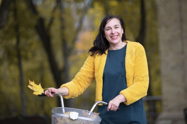 Happy middle-aged woman with bike in autumn park