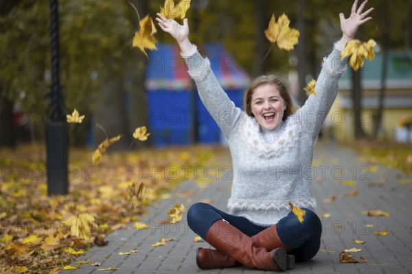 Beautiful girl in the autumn park scatters yellow leaves