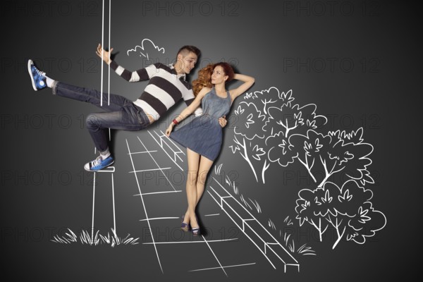 Happy Valentine's Day love story concept of a romantic couple against chalk drawings background. Male pole dancing on a lamppost while walking with girlfriend