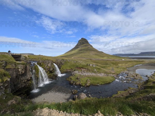 Landscape with a mountain and a waterfall flowing into a river under a blue sky with clouds. Iceland