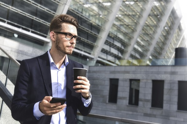 Handsome successful businessman in elegant suit outdoors stand at street in the city with coffee
