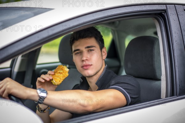 Young handsome man driving his car while eating food in the traffic
