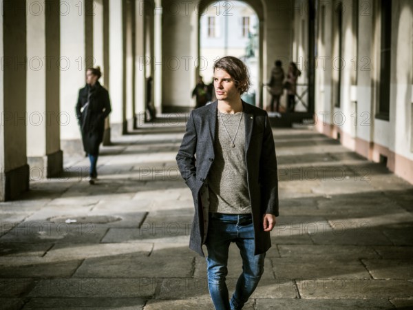 Elegant attractive young man outdoor wearing wool coat, in European city under colonnade in city center