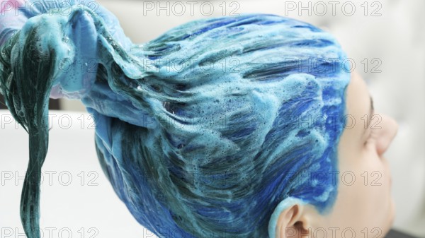 Professional hairdresser holds client's long blue hair in hand while washing hair after process of dyeing hair in beautiful dark blue color