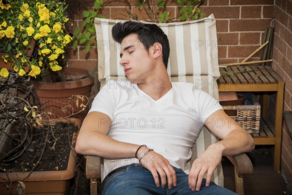 Handsome young man in balcony sleeping on chair wearing a v-neck white T-shirt while, in summer