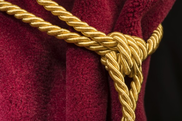 Red velvet curtain with tassel. Close up knot on rope