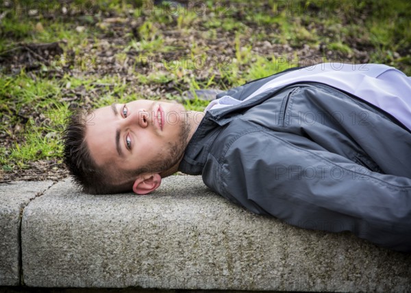 Portrait of handsome young man looking to a side while lying on bench in city park