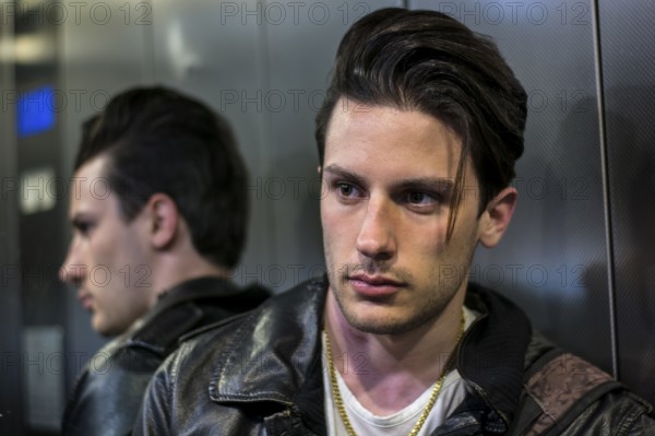 Handsome young man leaning against mirror inside an elevator or lift, looking at camera