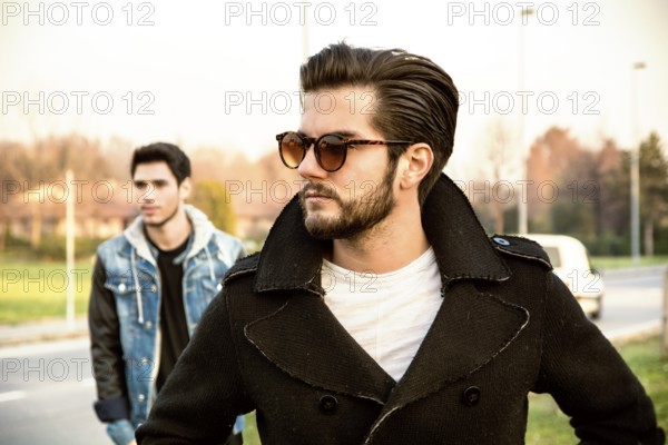 Two handsome casual trendy young men, 2 friends, in an urban park walking and chatting together