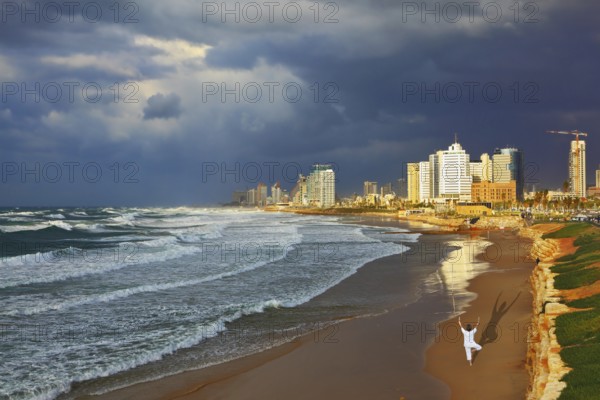 Storm cloud hanging over the sea, the woman in white performs yoga on one leg. Promenade and beach in Tel Aviv