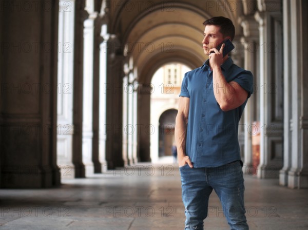 Handsome young athletic man standing outdoors in urban environment, talking on cell phone