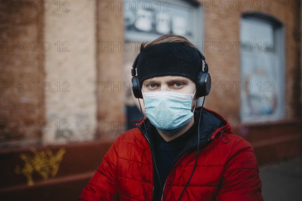 Man wearing a mask and headphones stands against a brick wall