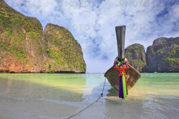 Scenic green islands of Thailand coast. Emerald sea and fine white sand. On the beach approached by a native boat for tourists, decorated with a red silk scarf