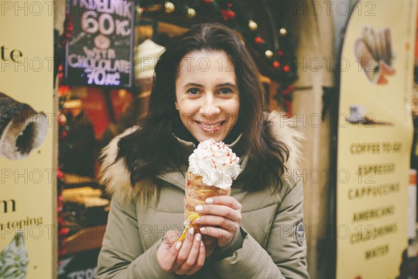 A beautiful girl in a warm jacket eats trdelnik or Trdlo with cream in her hands, in the winter in the Czech Republic, Prague at the Christmas market
