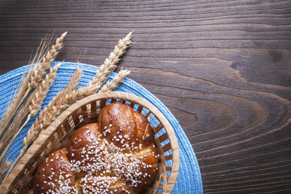 Sweet roll in wicker basket wheat rye ears with wattled table-cloth on wooden vintage board food and drink concept