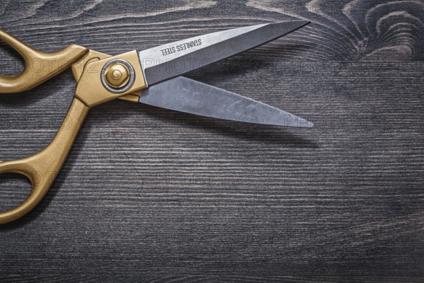 Pair of golden scissors on vintage wooden board top view