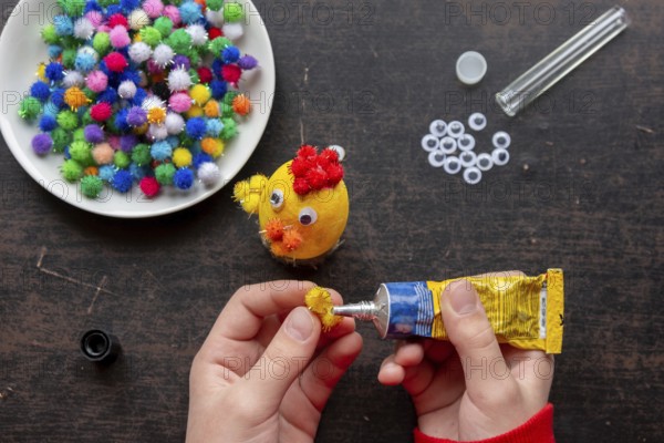 Children's hands glue the wing to the chicken figure with glue from a tube