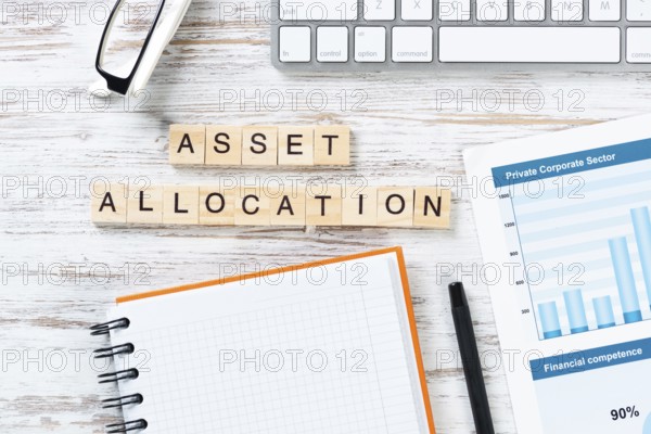 Asset allocation concept with letters on cubes. Still life of workplace with supplies. Flat lay vintage white wooden desk with computer keyboard and spiral notebook. Capital investment and management