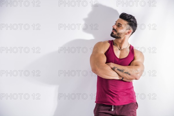 Muscular bodybuilder leaning against white wall, looking at it as if reading something, with large copyspace next to him