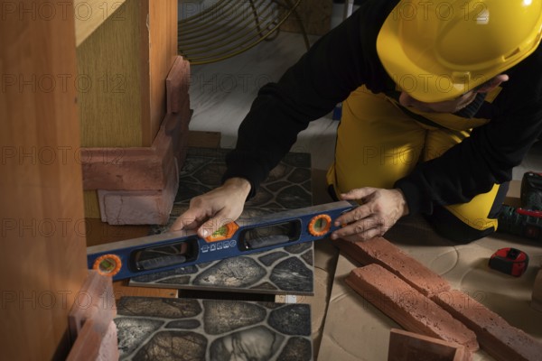 While laying the terracotta, the general construction worker checks the correctness of execution with a spirit level. An employee wearing personal protective equipment