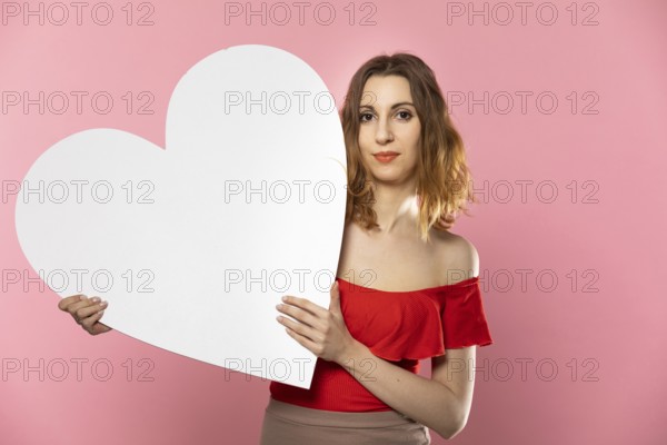 A beautiful girl in love holds a heart shape in her hand. Young woman wants to give a beautiful heart shape as a symbol of love on Valentine's Day