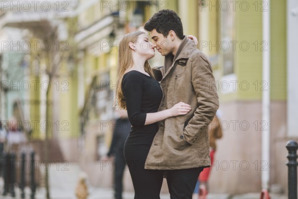 Urban modern young love couple walking romantic talking talking, holding hands on a date. Young multicultural Turkish brunette and Caucasian couple on old european street. Autumn spring weather