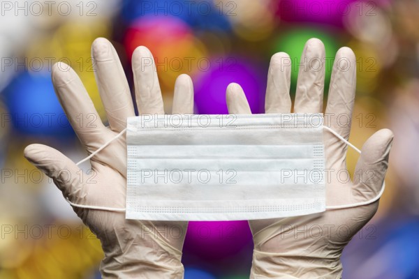 Doctor hands holding medical face mask in white gloves on background bokeh Happy New Years balls decorations. Concept of quarantine for Christmas festive due to coronavirus crisis covid-19 disease