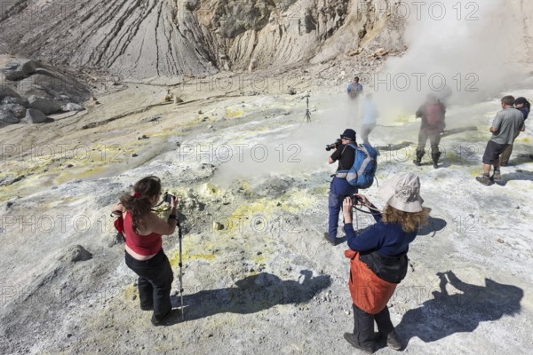 KAMCHATKA, RUSSIA, SEPTEMBER 11, 2013: Group photographers takes picture volcanic landscape, hot sprigs and active sulfur fumaroles, erupting steam and gas in crater of active Mutnovsky Volcano on Kamchatka